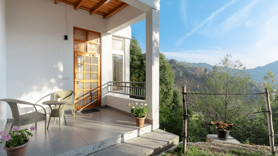 The front porch of Ziran Retreat, showing a sitting area with chairs and a table, overlooking a mountain landscape on a sunny day.