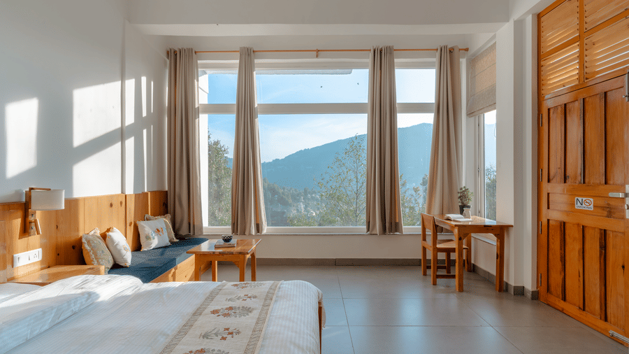 A bedroom at Ziran Retreat with a large bed, wooden furniture, and wide windows with a view of the mountains.