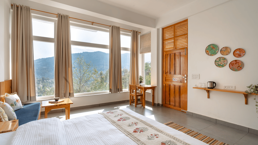 A bedroom at Ziran Retreat with a bed, a small sitting area, and large windows with a scenic view.
