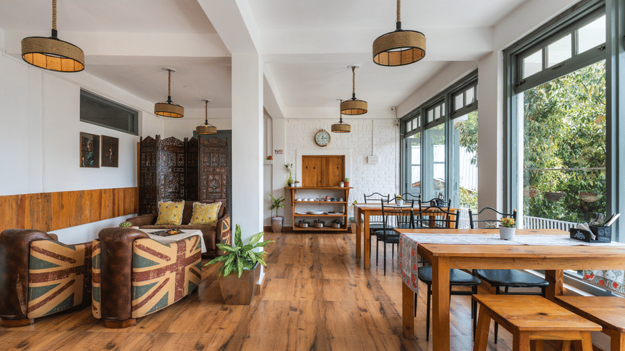 A close-up shot of Ziran Retreat's dining area, featuring a long wooden table with benches, and a small sitting area with striped armchairs, located near large windows.
