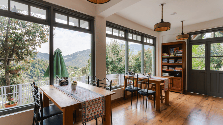 A dining area with tables and chairs next to a large window overlooking a patio at Ziran Retreat.