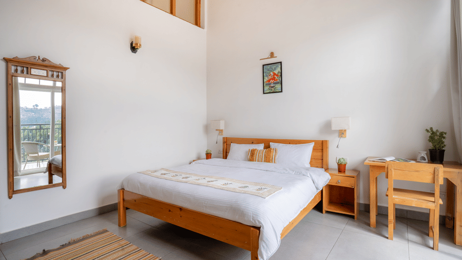 A bedroom at Ziran Retreat with a large bed, a wooden bedside table with a lamp, and a window with a mountain view.
