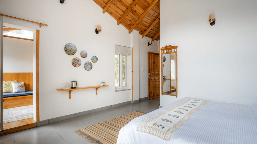 A bedroom at Ziran Retreat, showing a bed with a white comforter, a headboard with wall lamps, and a unique mirror and wall decor on the right side.