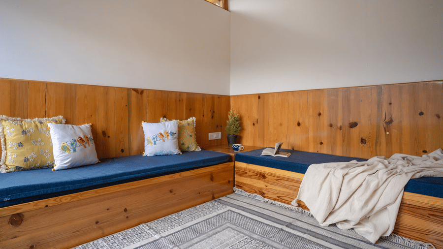 A close-up shot of the daybed area in Ziran Retreat's bedroom, showing the blue cushioned seat with colorful pillows, and the wooden paneling on the wall.