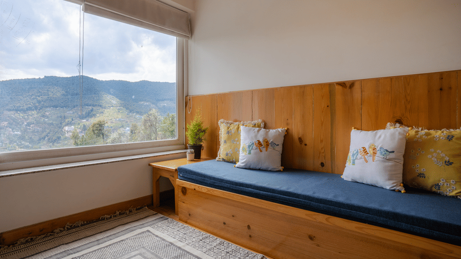 A room at Ziran Retreat with a sofa that doubles as a daybed, located in front of a wide window showing a mountain view.