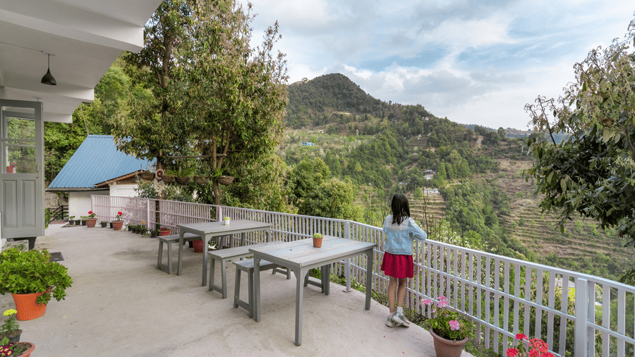A person standing on a chair on an outdoor patio with tables and a view of mountains at Ziran Retreat.