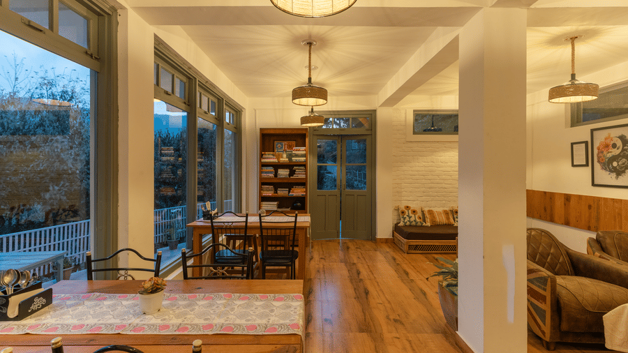 A wide shot of Ziran Retreat's main room, showing a living area with a sofa, a dining area with a table and chairs, and large windows looking out at the scenery.
