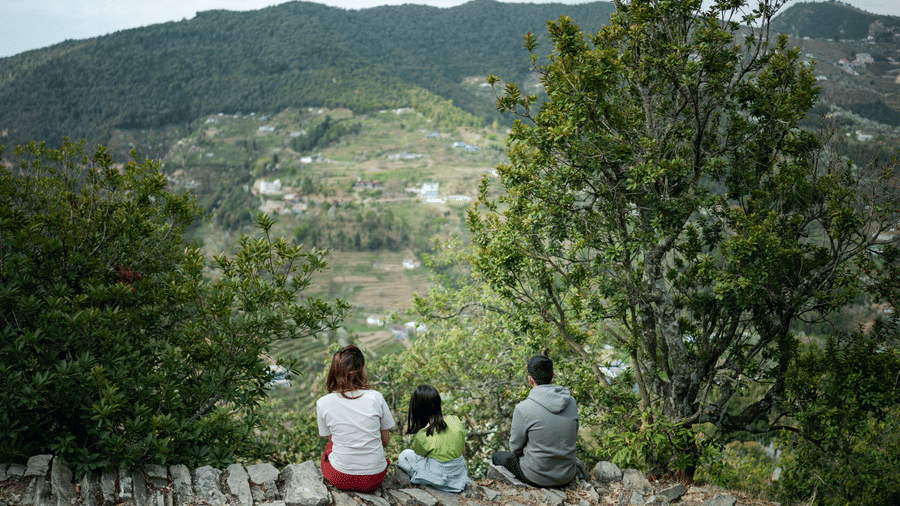 Three people are sitting on a stone wall overlooking a valley near Ziran Retreat.
