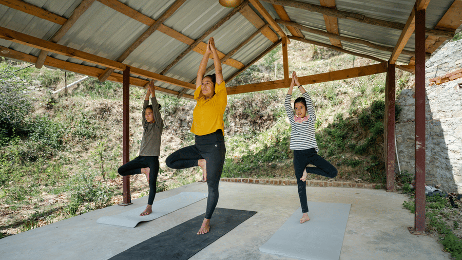 Two people are doing yoga poses on mats under a covered outdoor structure at Ziran Retreat.