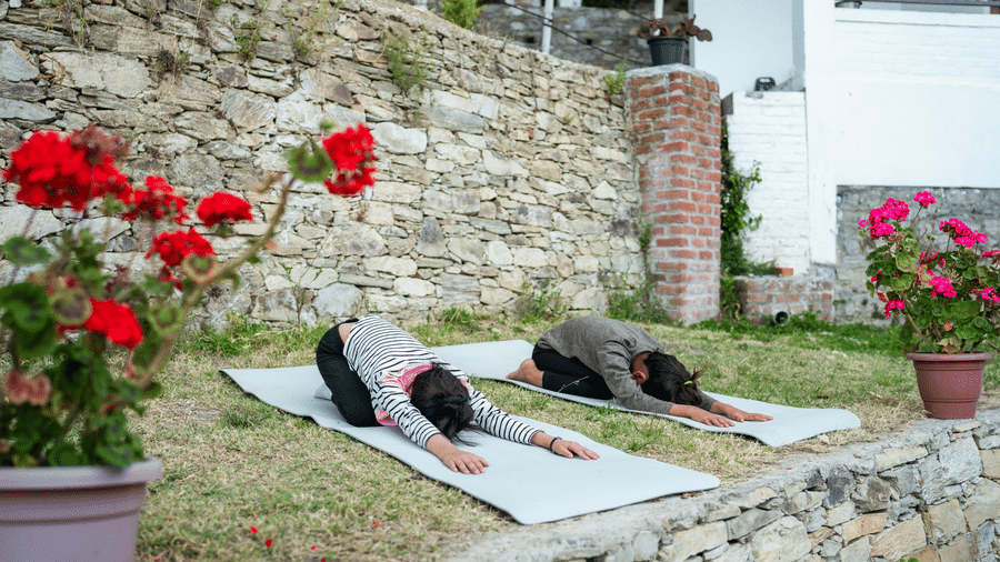 Two people are doing yoga on a grassy area in front of a stone building at Ziran Retreat.