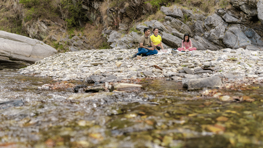 A long shot of 2 people sitting on a rocky riverbank near Ziran Retreat.