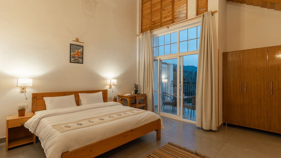 A bedroom at Ziran Retreat with a large bed, wooden furniture, and a floor-to-ceiling window looking out at a scenic view.