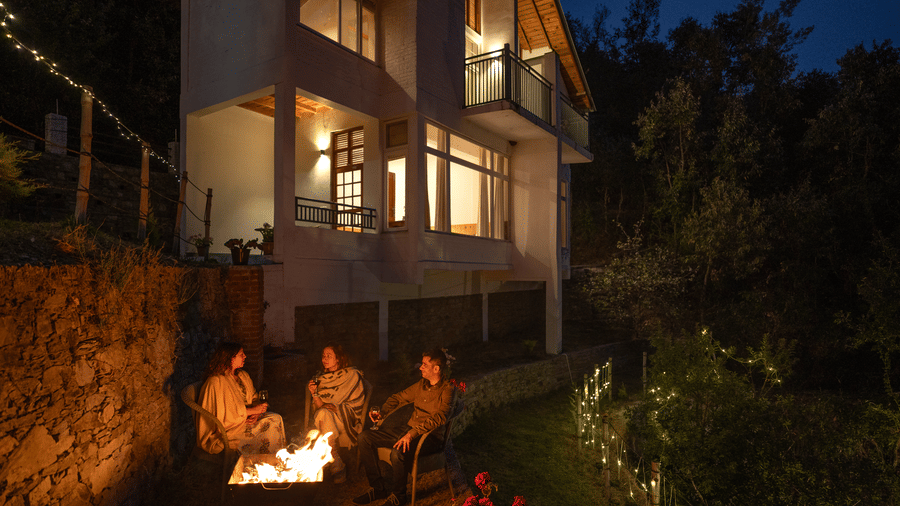 A group of people are sitting around a bonfire in front of a multi-story building at Ziran Retreat.