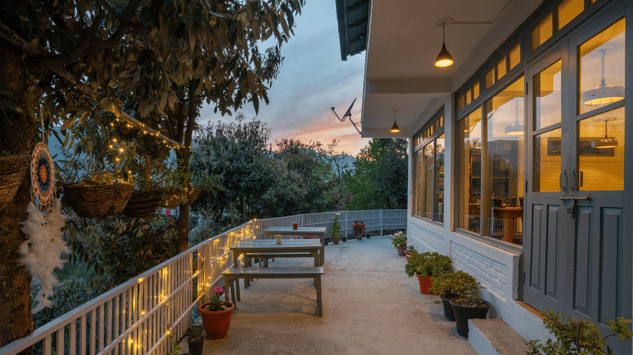 An outdoor shot of the Ziran Retreat terrace area at dusk, with wooden benches and tables and lighting on the walls, overlooking a scenic view.