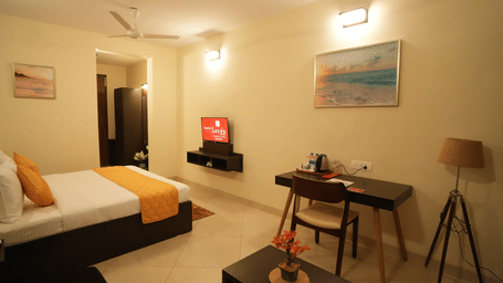 A double bed room with paintings, ceiling fan, lamp and work desk with chair