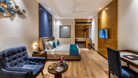 Modern executive room with blue sofas, queen bed, and wood flooring.