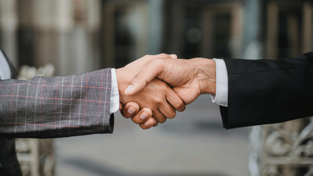 A man and a woman in business suits are shaking hands, in what appears to be a professional setting.