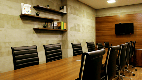 A modern conference room with a large wooden table and chairs, and a wall-mounted TV.