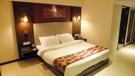 A warmly lit standard hotel room of Lords Plaza Surat featuring a double bed and wooden panelled head-rest