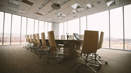 A spacious boardroom with a long wooden table, high-backed office chairs, and floor-to-ceiling windows