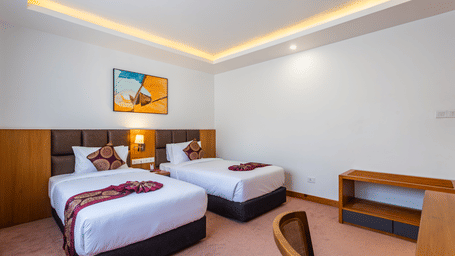 Two double beds, with lamps on the side, a desk and a chair