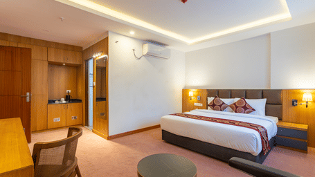 A single bed, TV and seating area with window and curtains, coffee station and door to bathroom in our hotel rooms in Kathmandu.