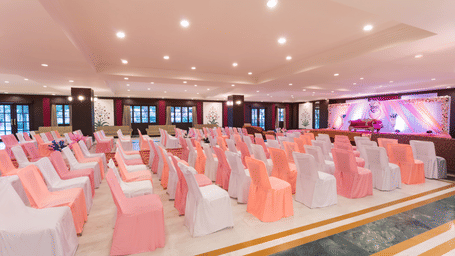 Rows of banquet chairs in white and peach covers arranged for an event in a spacious well-lit Raj Mahal at Shri Vallabh Villas Lords Plaza Nathdwara.
