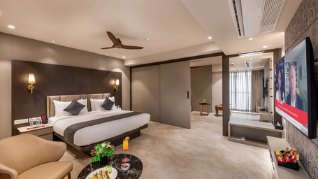 A stylishly appointed bedroom of the Suite with a double bed, seating area facing the wall-mounted television, and neutral decor – Skkylight Lords Inn, Nanded