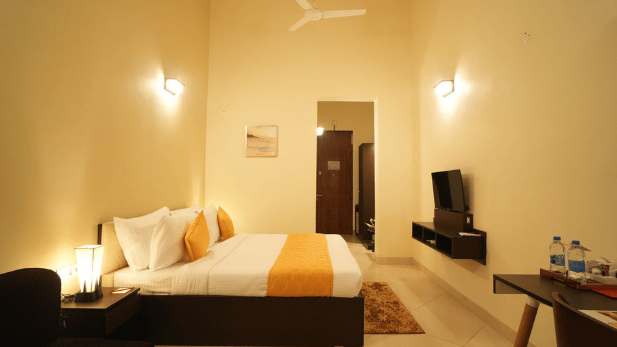 A wide view of a double bed room wit ceiling fan, paintings,TV and table with water bottles on it