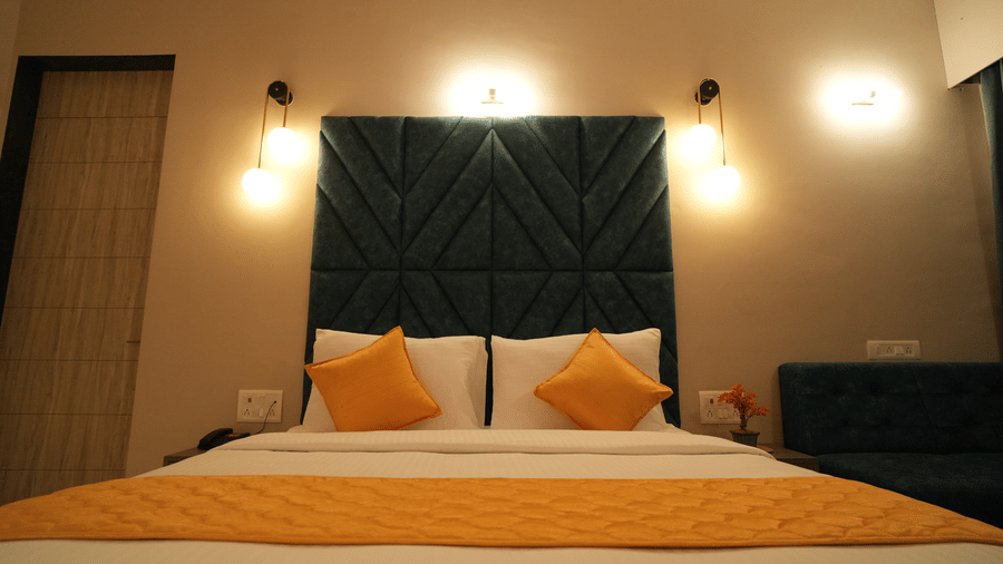 A double bed with pillows and bedsheets, bed posts and lamps on the wall