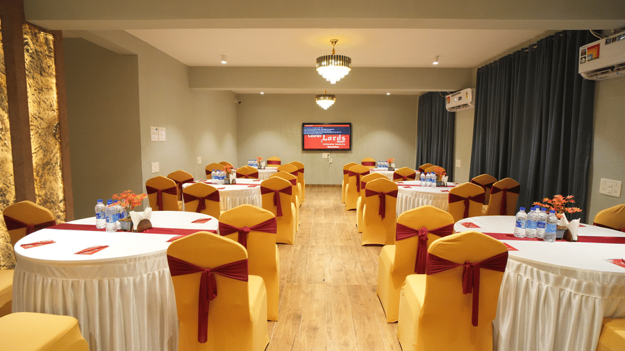 A class room style seating area with tables and chairs, TV and chandelier lighting 