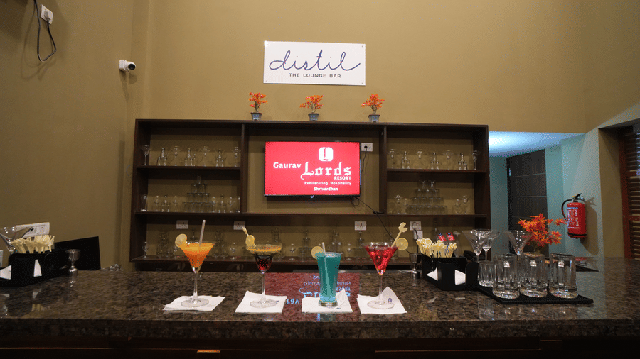 Bar counter with granite top showcasing colourful mocktails, cocktail glasses, napkins, and stirrers, backed by wooden shelves filled with glassware and minimal décor - Gaurav Lords Resort Shrivardhan
