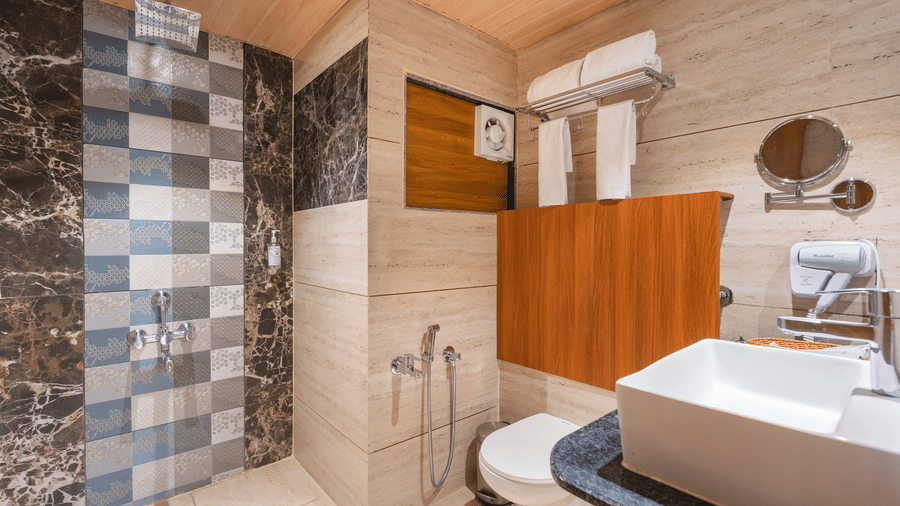 A modern bathroom features a rectangular sink, a toilet, and a shower area with patterned tiles - Lords Eco Inn Ambaji.