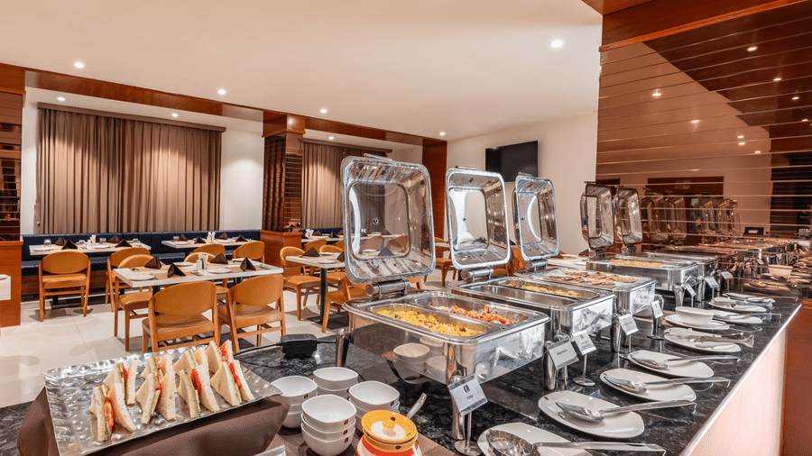 A buffet spread with covered food warmers, plates, and other serving dishes is ready in a dining area - Lords Eco Inn Ambaji.