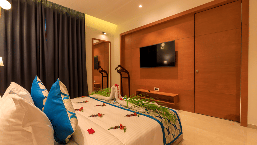 A warmly lit Executive Room at Lords Eco Inn Apple Gate features a decorated double bed, a wall-mounted TV, and dark curtains.