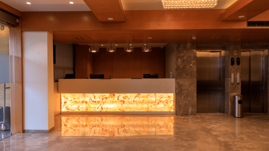 The warmly lit reception area of what appears to be Lords Eco Inn Apple Gate features a modern front desk, marble flooring, and elevators.