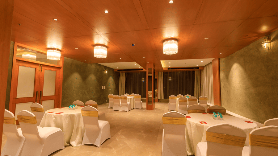 A warmly lit banquet hall at Lords Eco Inn Apple Gate is set with round tables draped in white, surrounded by chairs with gold sashes.