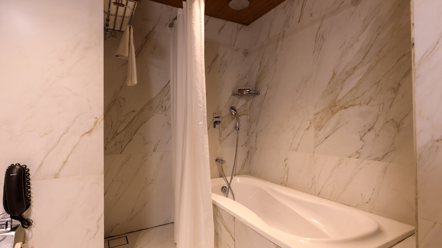 A modern bathroom at Lords Eco Inn Apple Gate features a bathtub with a shower curtain and marble-effect wall tiles.