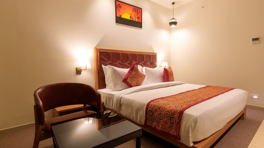 A warmly lit hotel room at Lords Eco Inn Apple Gate features a double bed with patterned accents, a chair and a small table.