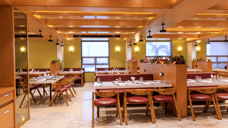 The well-lit restaurant at Lords Eco Inn Apple Gate features set tables with chairs, wooden accents, and natural light from windows.
