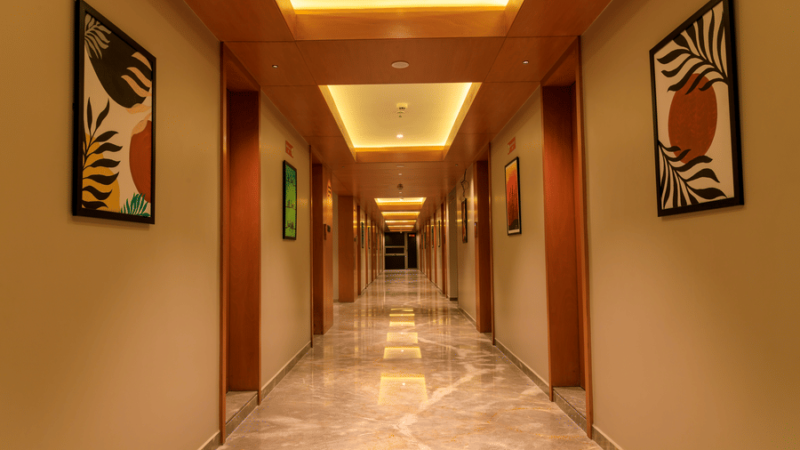 A brightly lit corridor at Lords Eco Inn Apple Gate features marble-effect flooring, artwork on the walls, and multiple room doors along its length.
