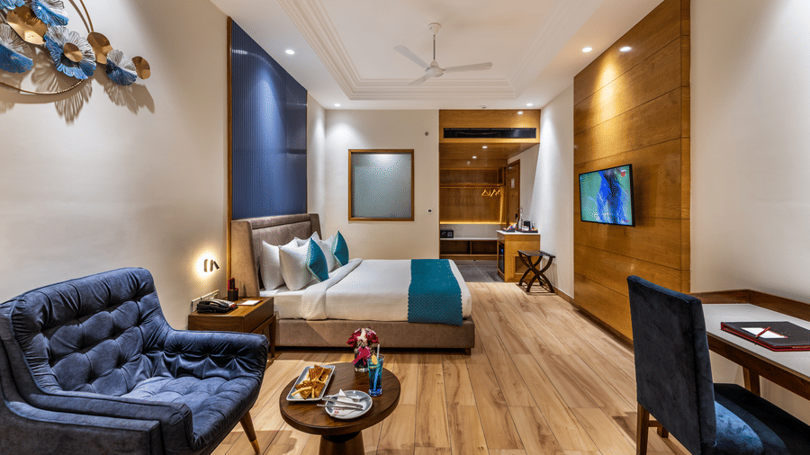 Modern executive room with blue sofas, queen bed, and wood flooring.