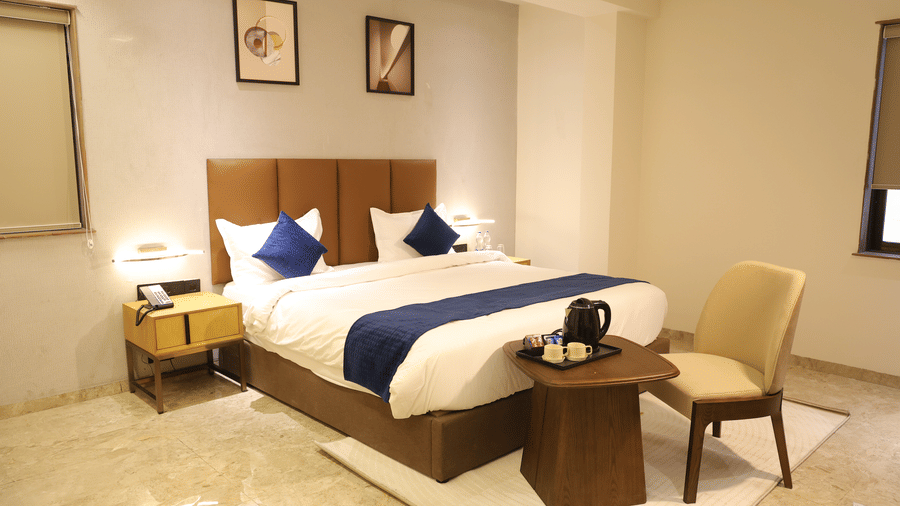 A spacious Deluxe Room at Lords Studio Inn, Jamnagar with a large bed two bedside tables and modern artwork.