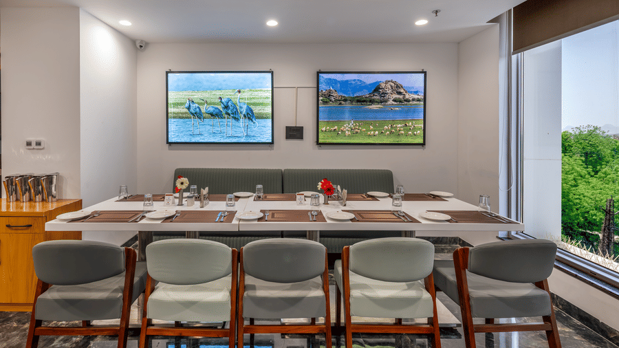 Modern dining area in BCR Resturant with cushioned seating, nature-themed wall art, large windows, and a neatly set table for a group meal