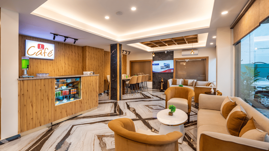 A reception waiting area at Lords Inn Katra showcases upholstered armchairs, a wall-mounted television, and a wooden counter.