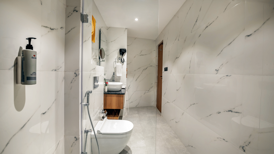 Modern bathroom at Lords Inn Katra with marble walls, wall mounted toilet, and vanity sink.