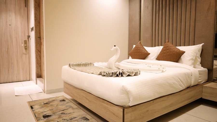 An angled view shows a tidy double bed decorated with a folded swan towel - Lords Inn Sangam, Bhopal