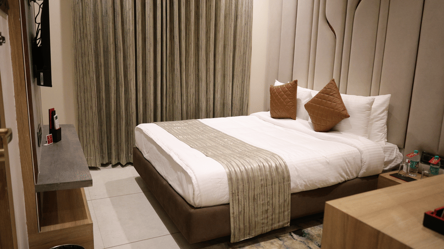 A neatly made bed is positioned opposite a window with long curtains - Lords Inn Sangam, Bhopal