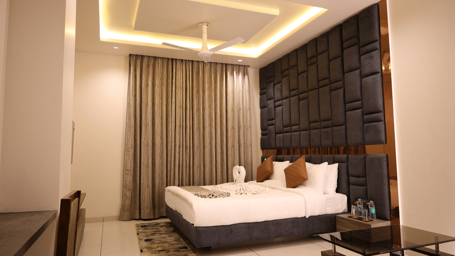 A large double bed sits below a decorative dark panelled wall with warm lighting - Lords Inn Sangam, Bhopal