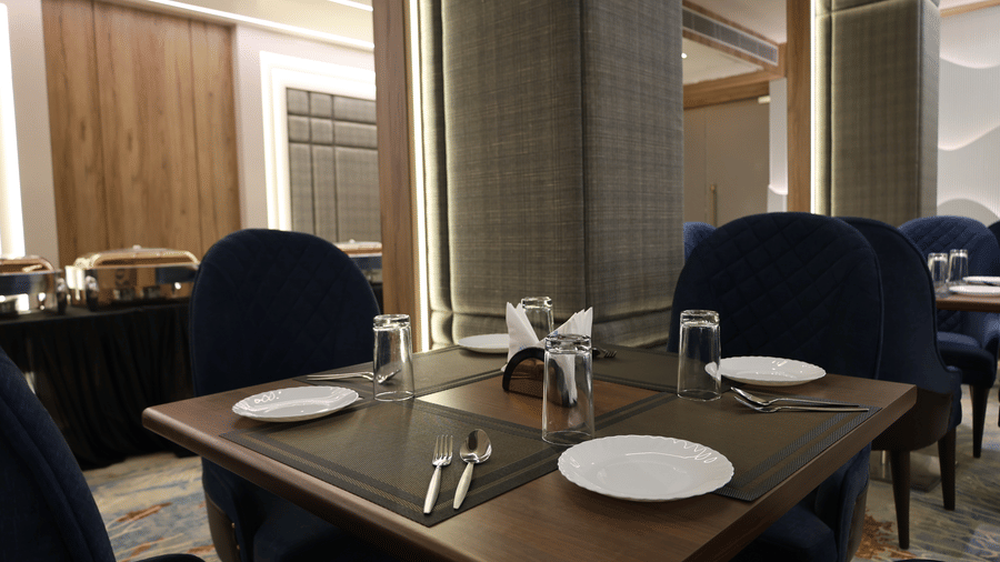 A neatly set wooden dining table is surrounded by plush blue velvet chairs - Lords Inn Sangam, Bhopal
